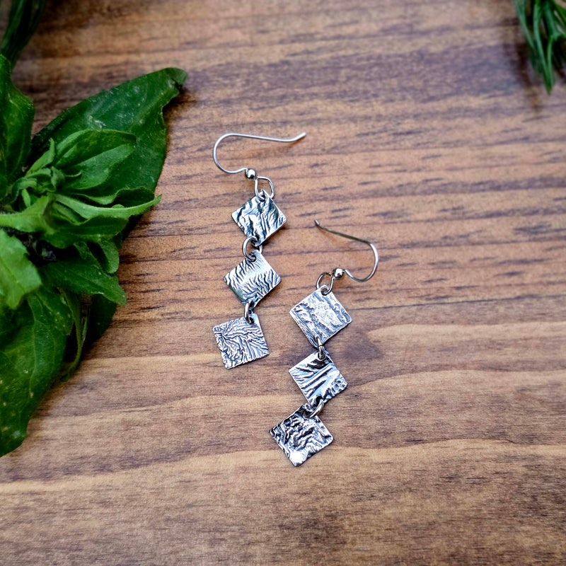close-up of reticulated silver drop earrings with three diamond-shaped elements