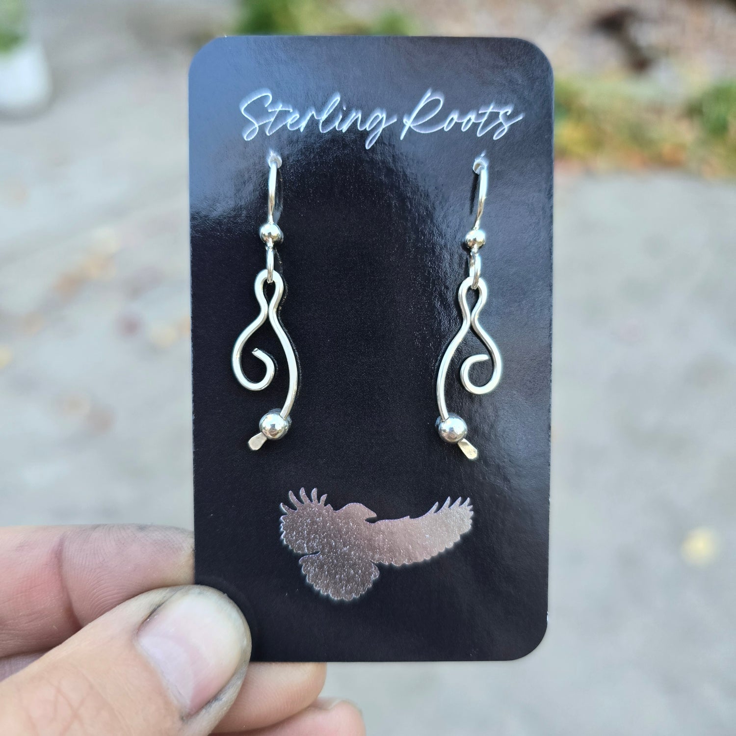 Silver earrings on a black card held by a hand with a blurred background