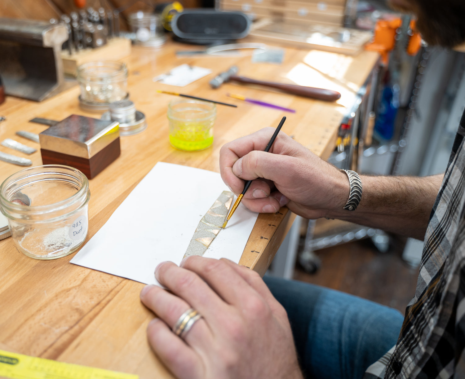Silversmith measuring argentium silver while forging a cuff by hand.