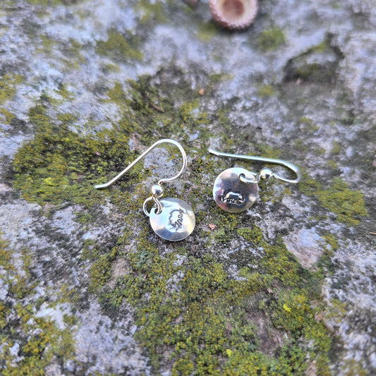 silver bear stamped earrings displayed on mossy rock