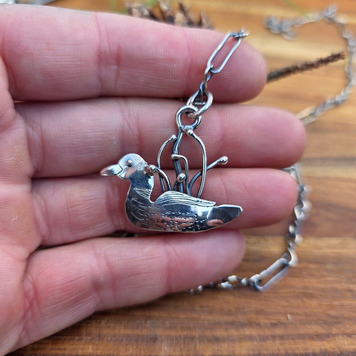 Silver bird-shaped pendant on a chain held in a hand against a wooden background
