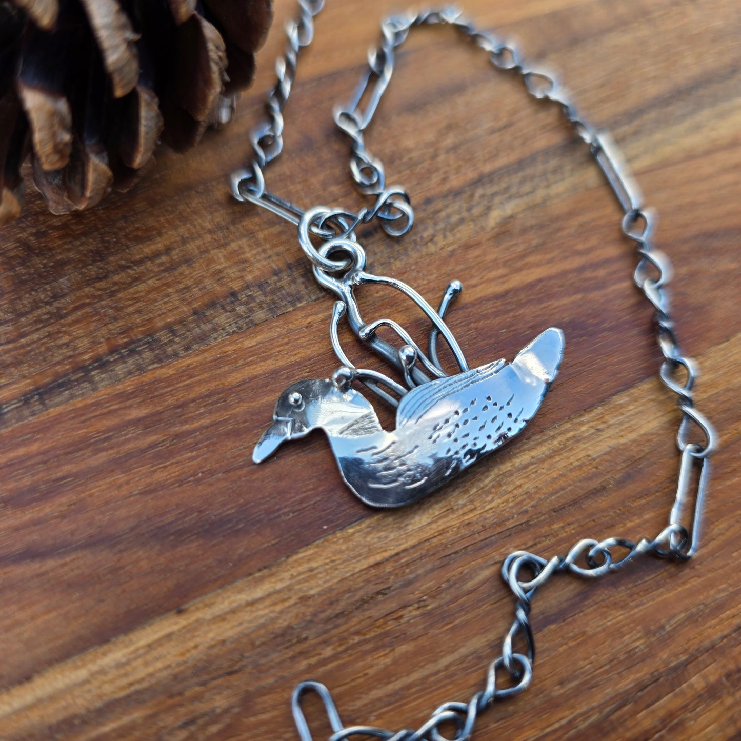 Sterling silver loon bird pendant on chain displayed on wooden background