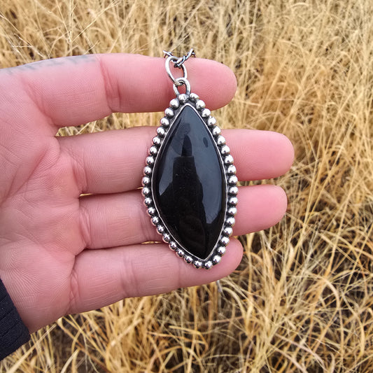 Sterling and black obsidian pendant displayed in hand with natural background front view