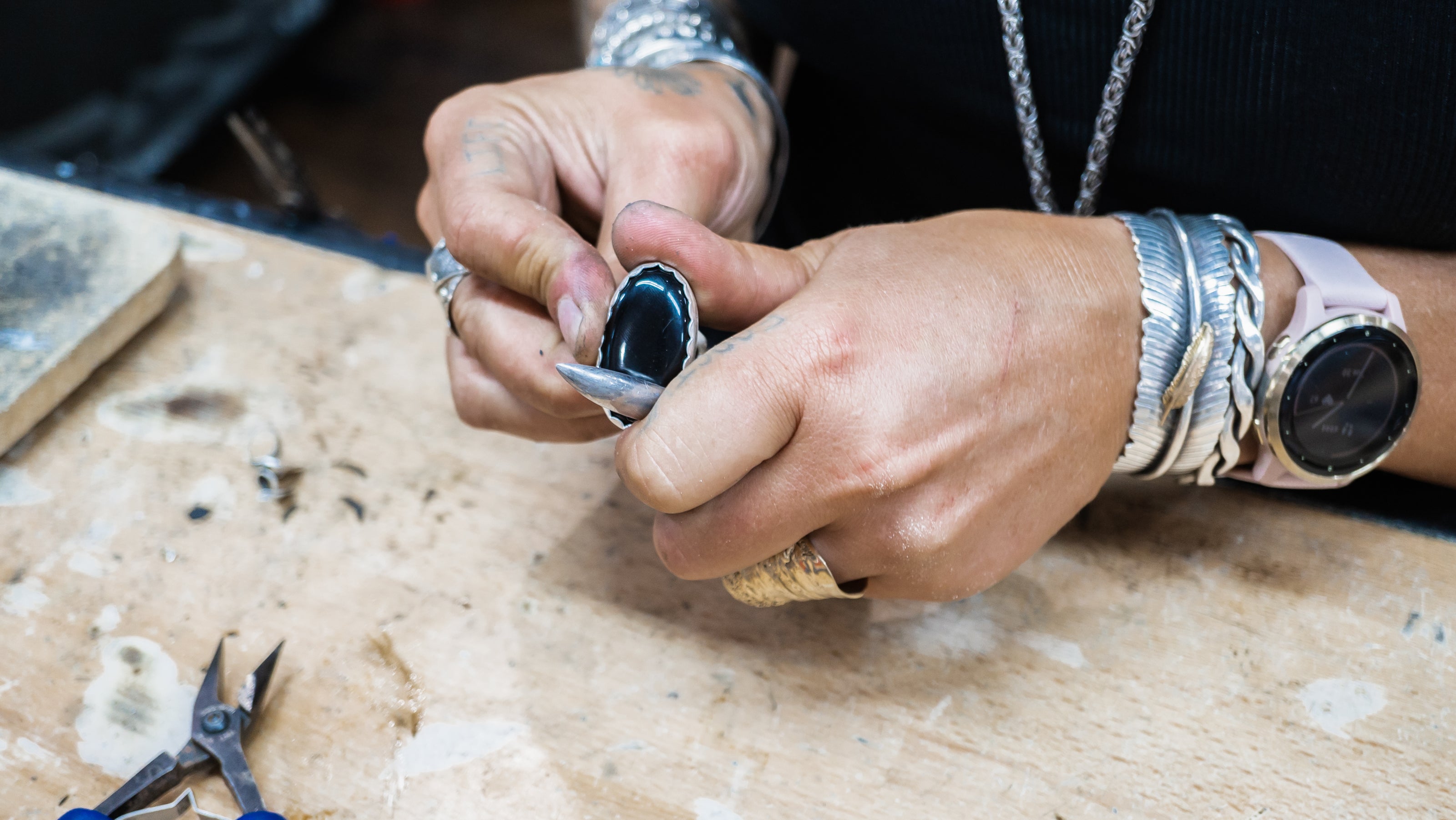 Silversmith using traditional stone setting tools at workbench while forging jewelry by hand.