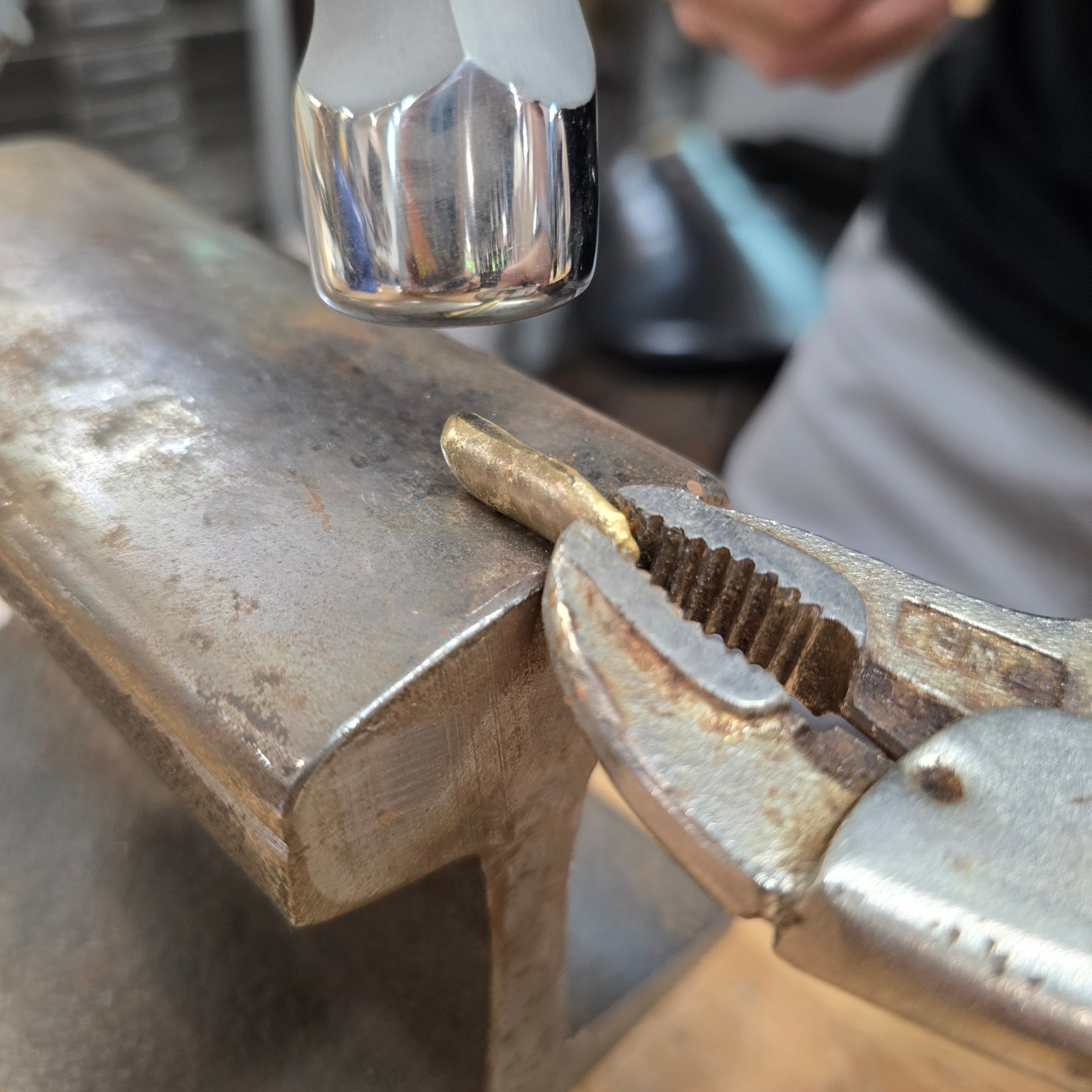 Silversmith forging 18k gold bar using traditional hammer and anvil while forging gold jewelry in Sterling Roots Studio.