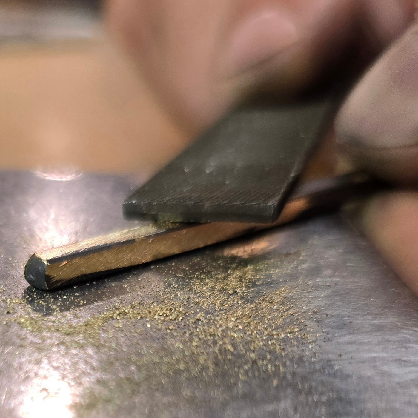 Silversmith filing 18k gold while forging jewelry by hand on anvil.