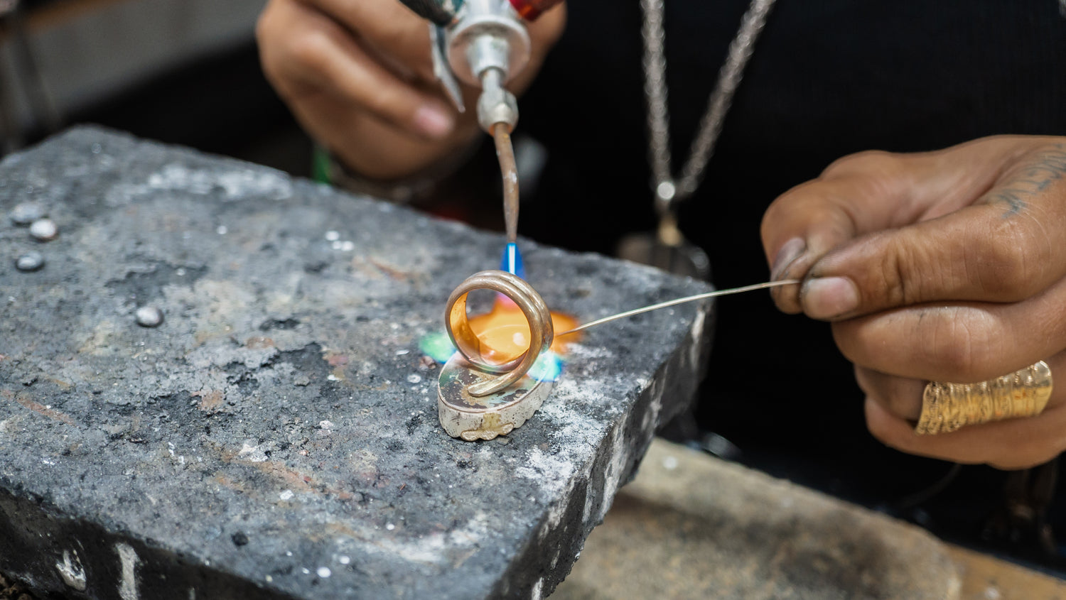Silversmith soldering a ring shank using traditional tools while forging sterling silver jewelry in Adirondacks.