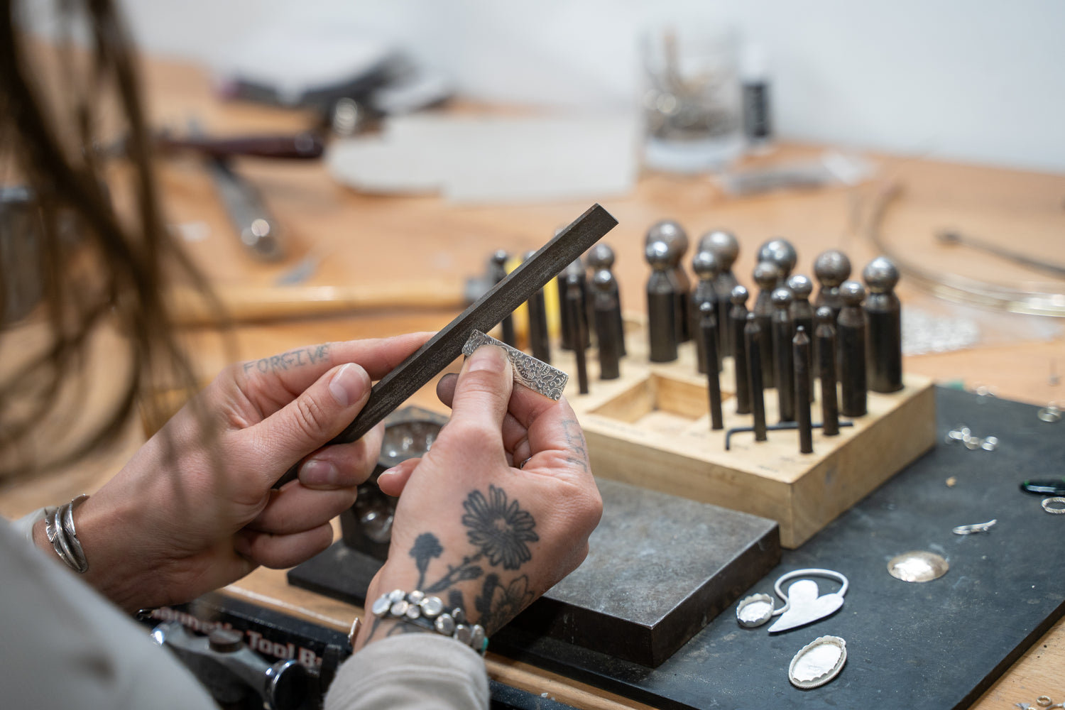 Close up of silversmith at Sterling Roots Studio using traditional silversmithing files to form sterling silver into jewlery with daping block in background.