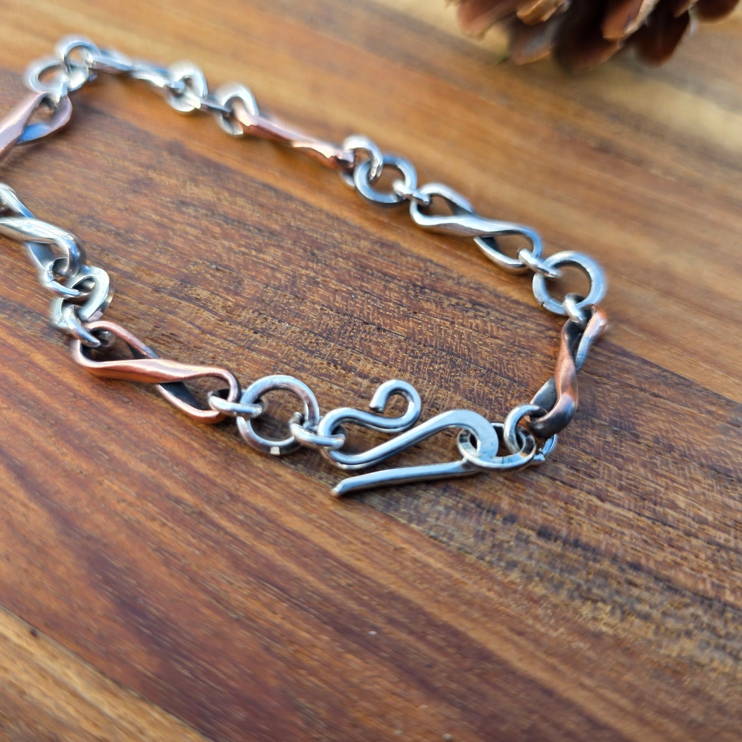 Oxidized alternating copper and sterling silver infinity link bracelet made from half round wire, shown with a silver clasp against a natural background.
