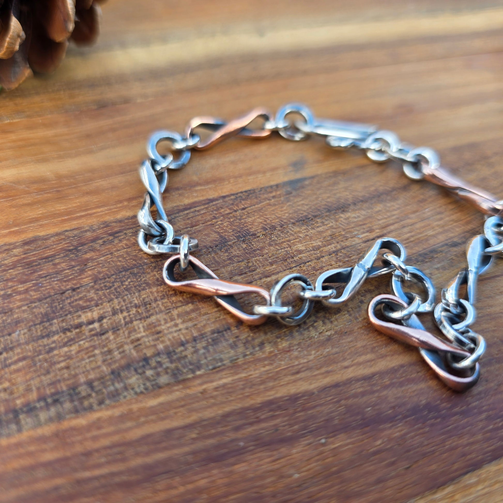 Infinity link bracelet featuring alternating copper and sterling silver half round wire links, oxidized for contrast, photographed with its clasp in a natural environment.