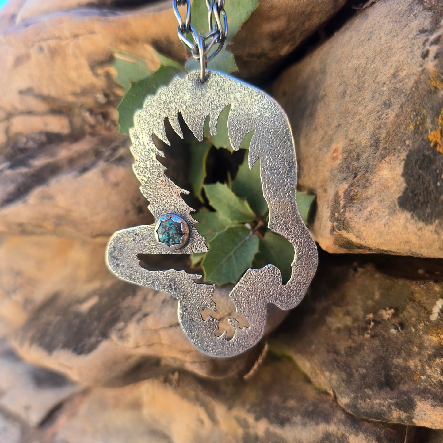 Sterling silver raven pendant with an oxidized finish, textured surface, and a small turquoise accent, measuring just over 3.5 inches in length with a large bail attached.