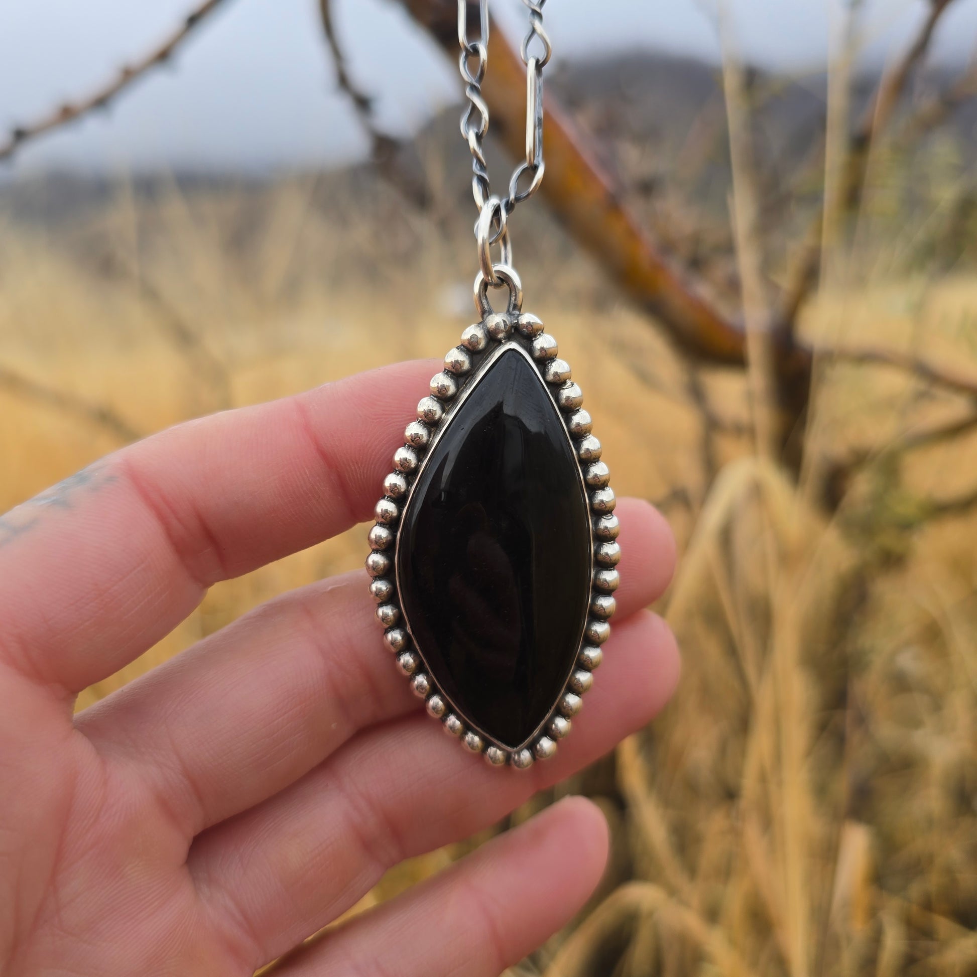 Sterling and black obsidian pendant on chain with natural background and hand front fiew