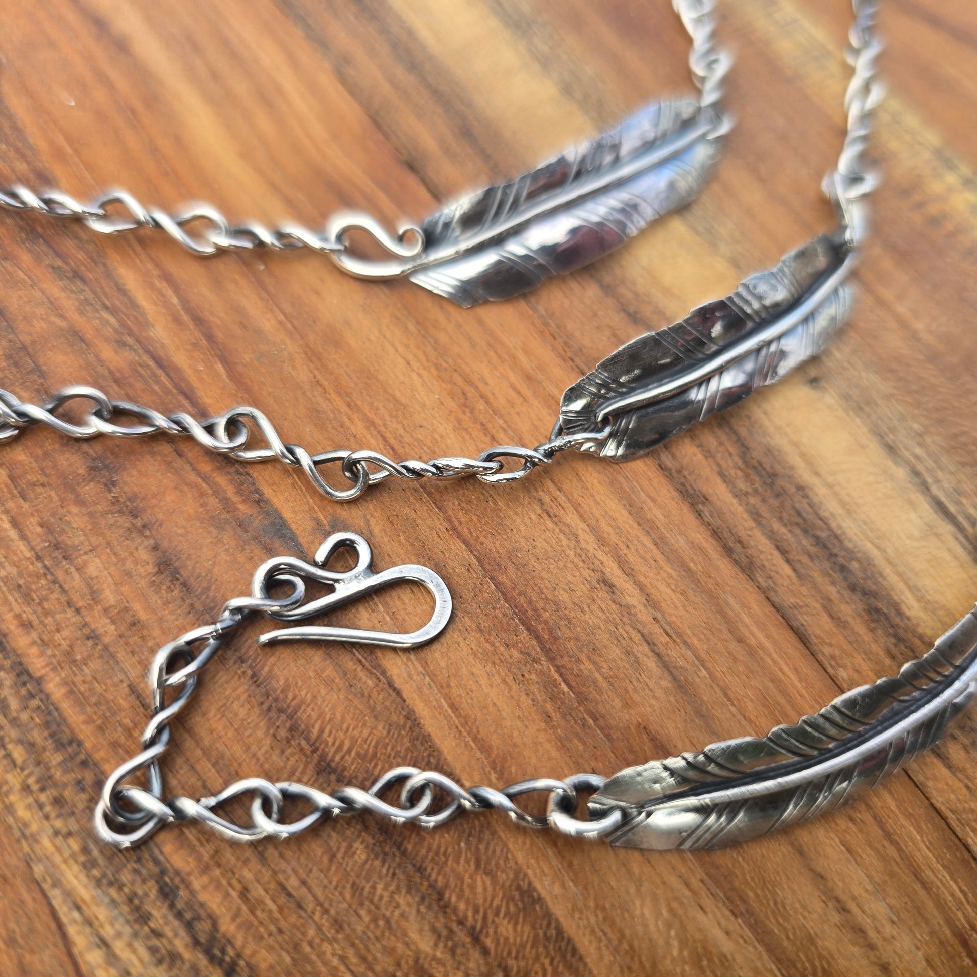 collection of sterling silver feather bracelets angled view on wooden surface