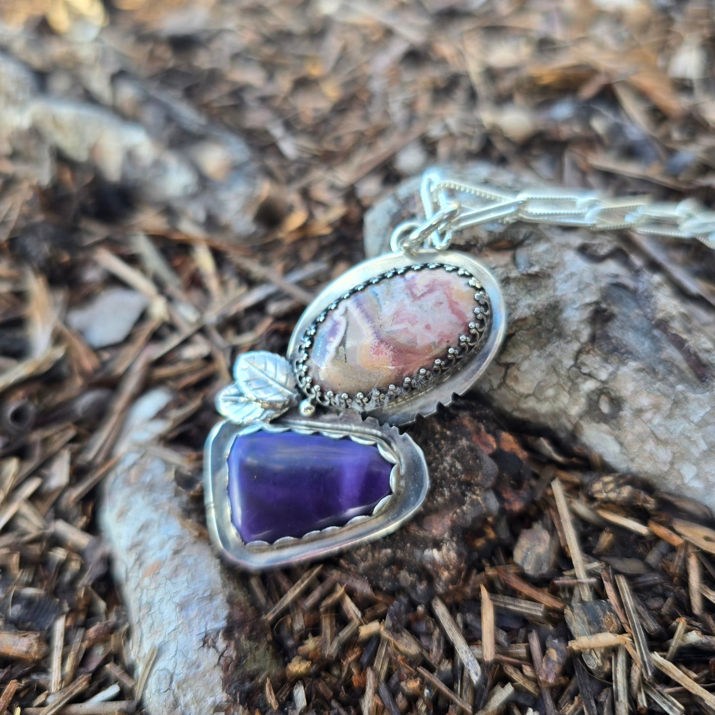 silver leaf pendant with purple tiffany jasper and pink stone displayed on ground