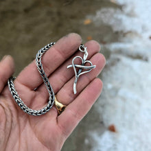 Load image into Gallery viewer, Sterling silver cross pendant with an intertwined heart at the center, shown with a smooth metal surface and attached bail displayed on hand
