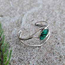 Load image into Gallery viewer, Top angled view of a sterling silver cuff bracelet set with an oval malachite stone and finished with a polished surface.

