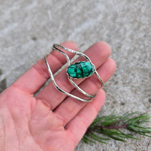 Load image into Gallery viewer, Front view of a sterling silver cuff bracelet set with an oval malachite stone and finished on a hand.
