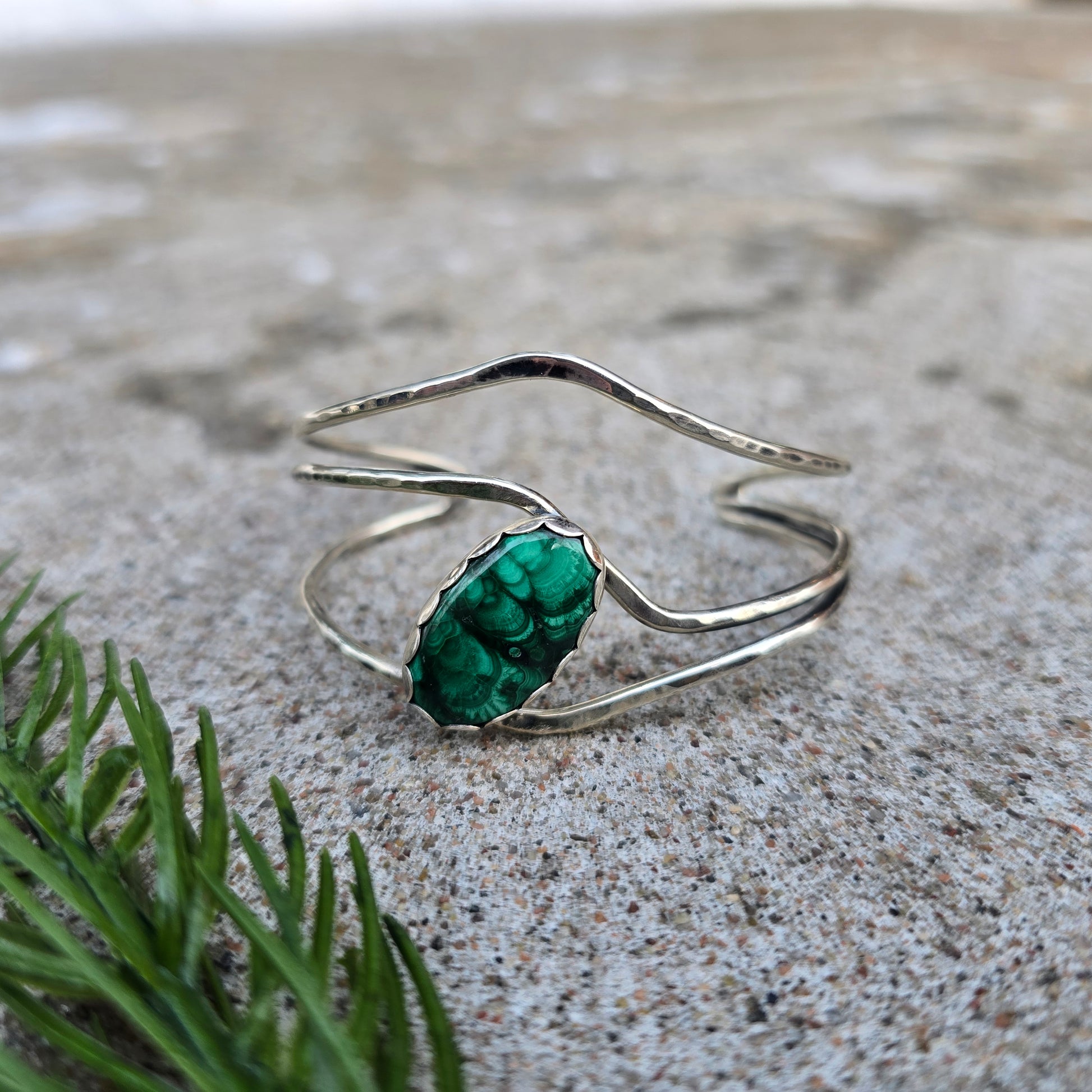 Front view of a sterling silver cuff bracelet set with an oval malachite stone and finished with a polished surface.