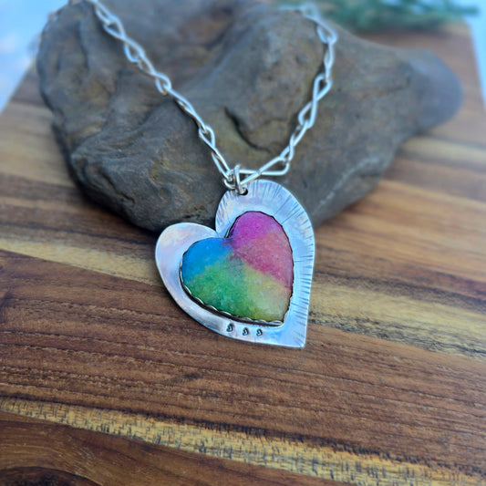 Top view of a heart-shaped sterling silver pendant set with rainbow quartz and finished with an oxidized surface.
