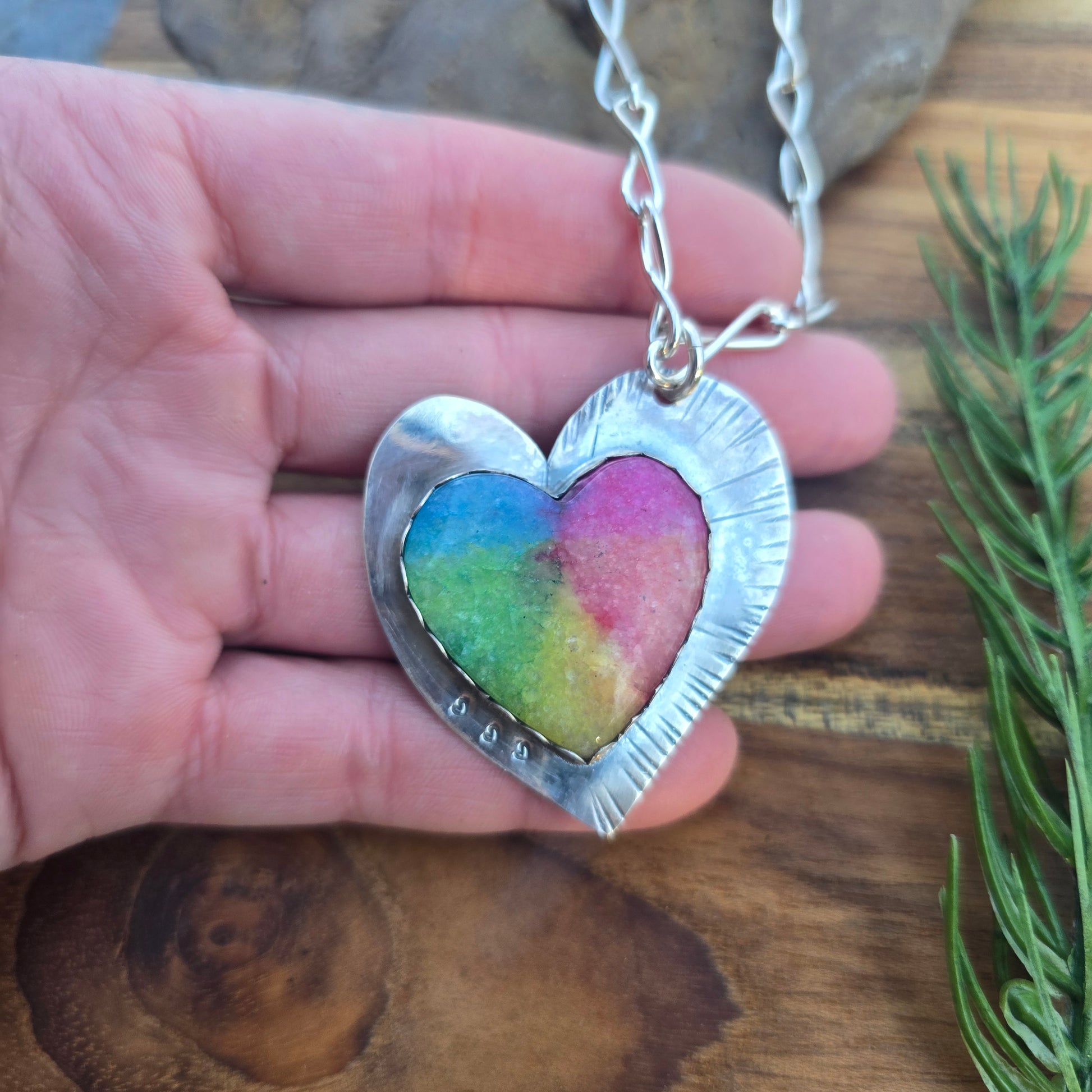 Top view of a heart-shaped sterling silver rainbow quartz pendant showing on hand