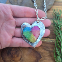 Load image into Gallery viewer, Top view of a heart-shaped sterling silver rainbow quartz pendant showing on hand

