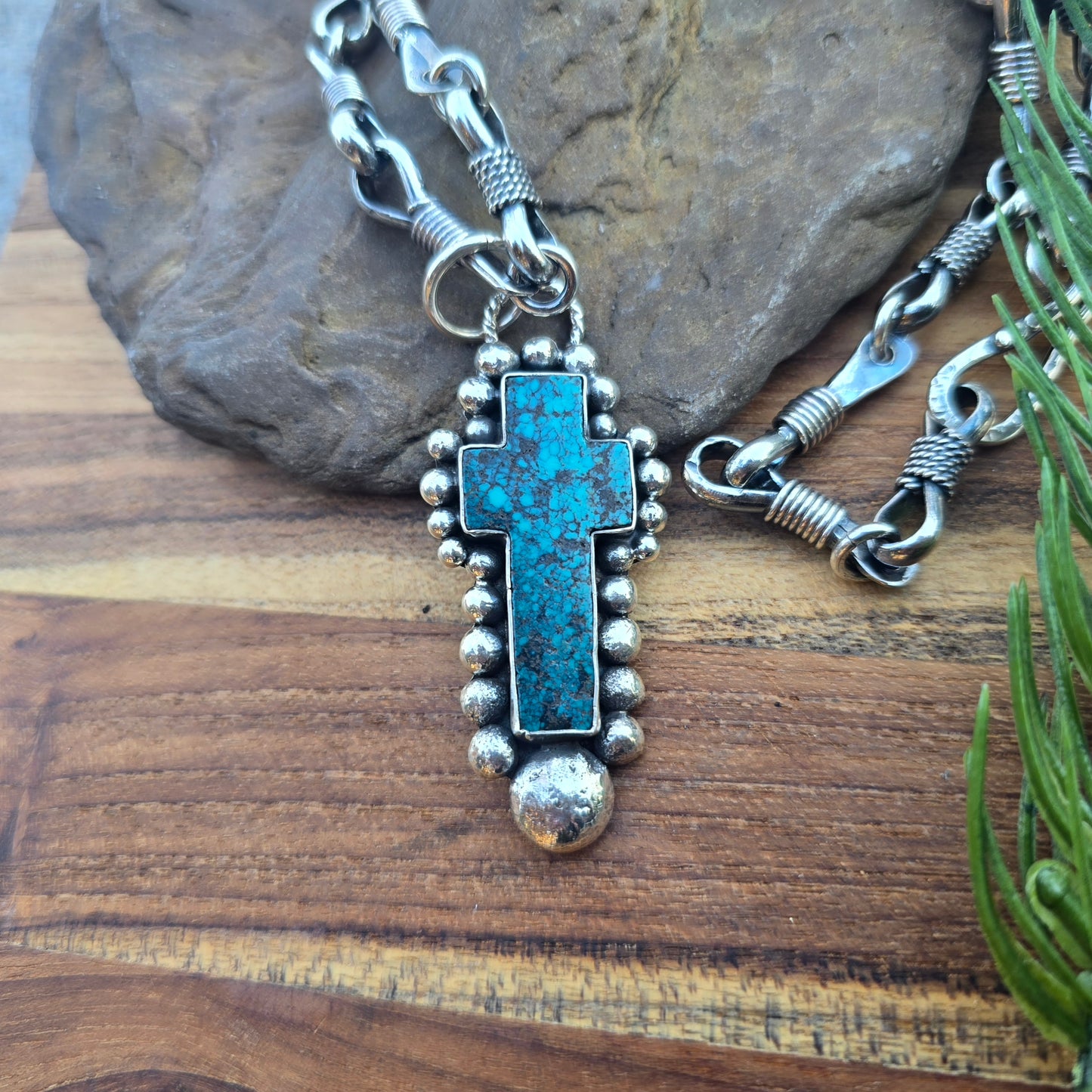 Top view of a sterling silver cross pendant with beaded detailing, set with turquoise and finished with an oxidized surface.
