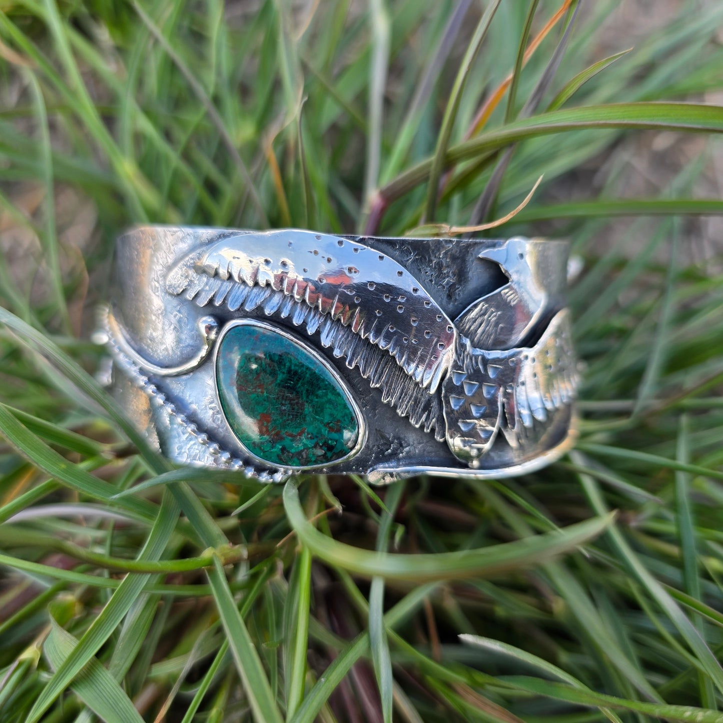 silver loon wing bracelet with green stone front view on grass