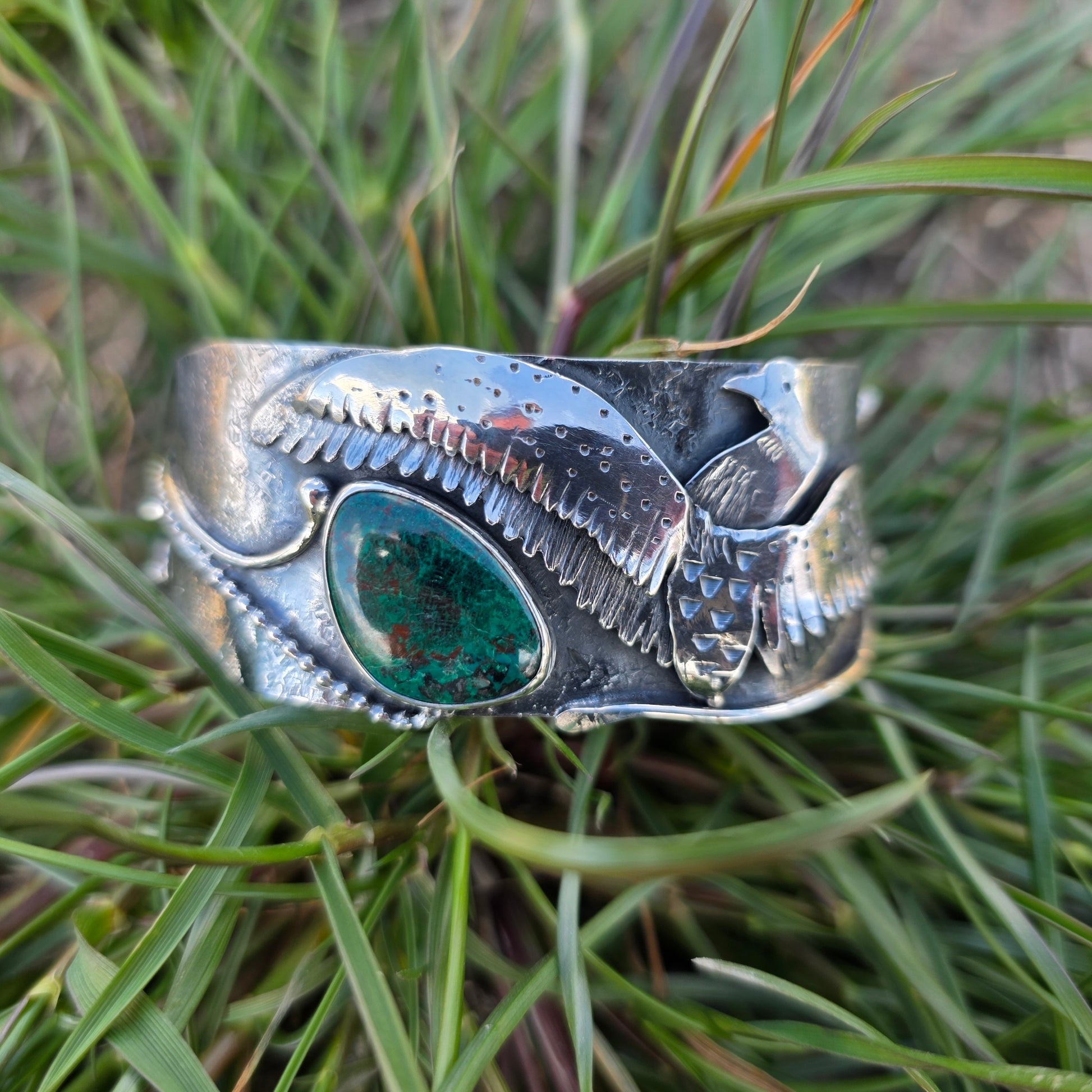silver loon wing bracelet with green stone front view on grass