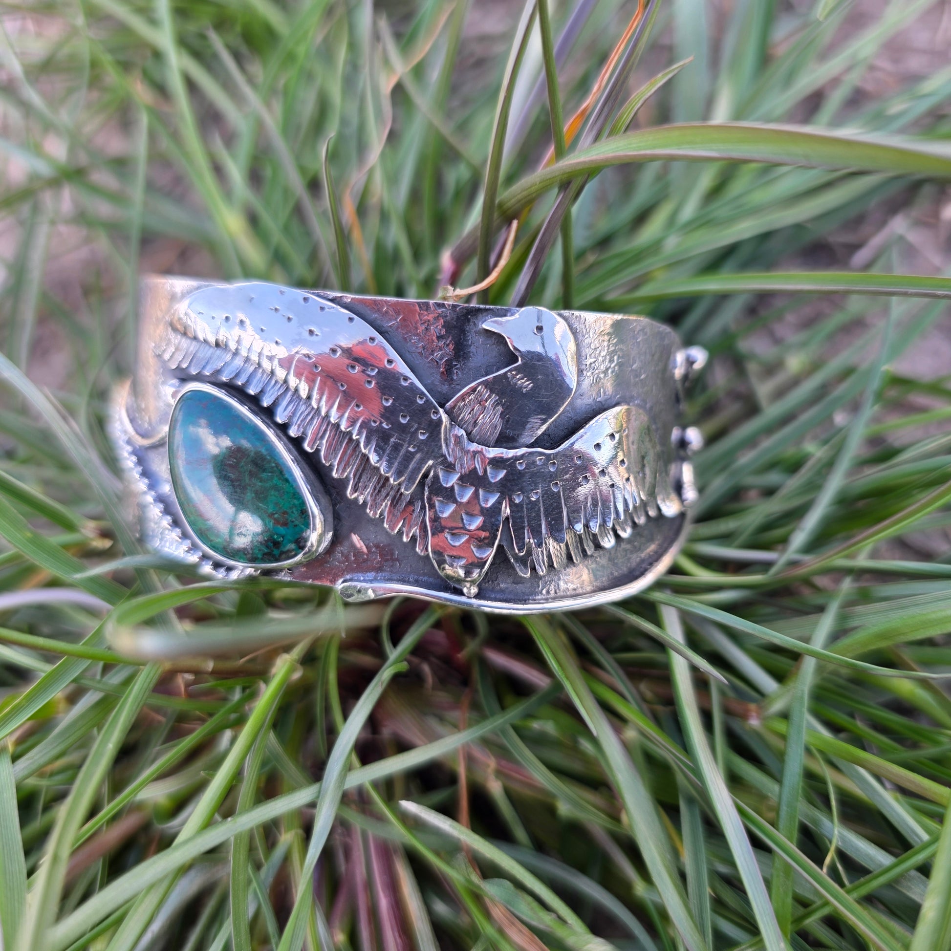 Sterling silver loon wing bracelet with green stone displayed on grass