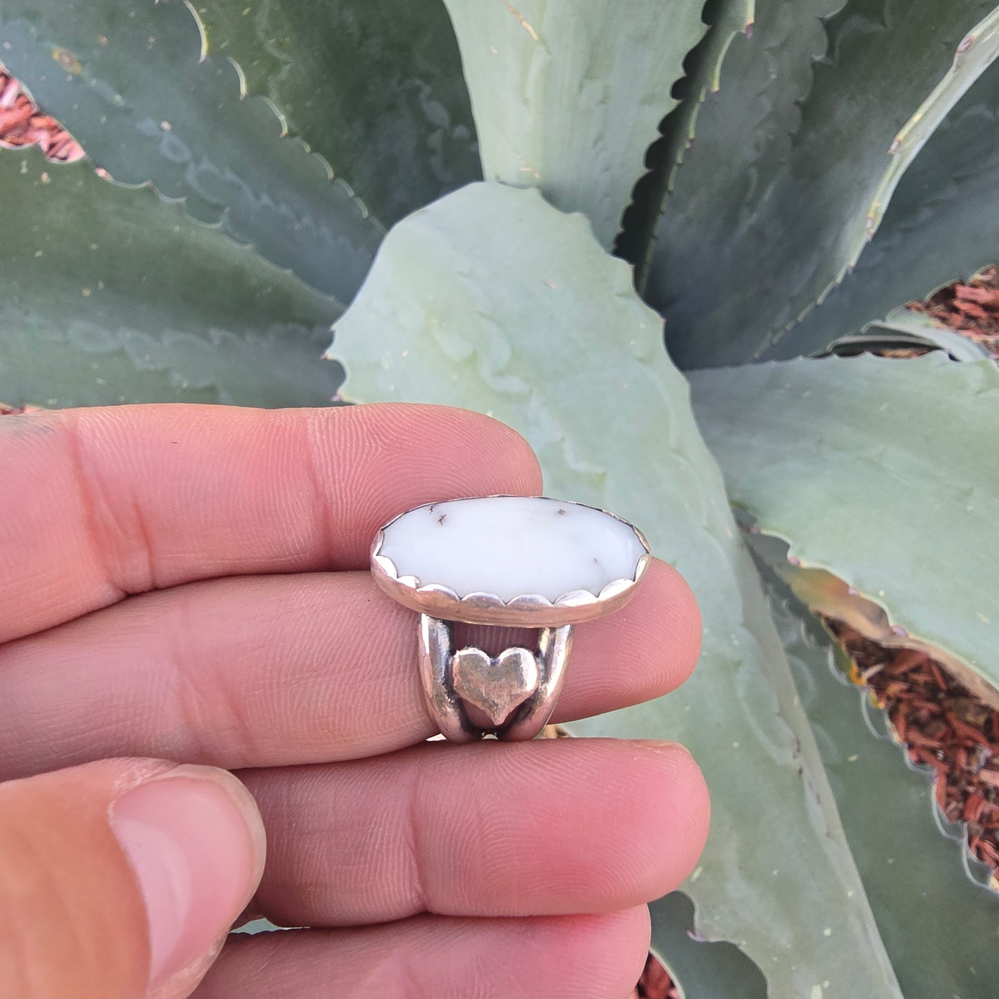 Sterling silver and white ring displayed on finger on natural background.