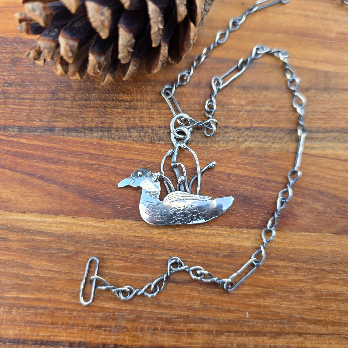 Sterling silver Adirondack loon pendant on chain displayed on wooden background