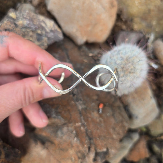 Polished sterling silver infinity cuff bracelet photographed flat against a natural background.
