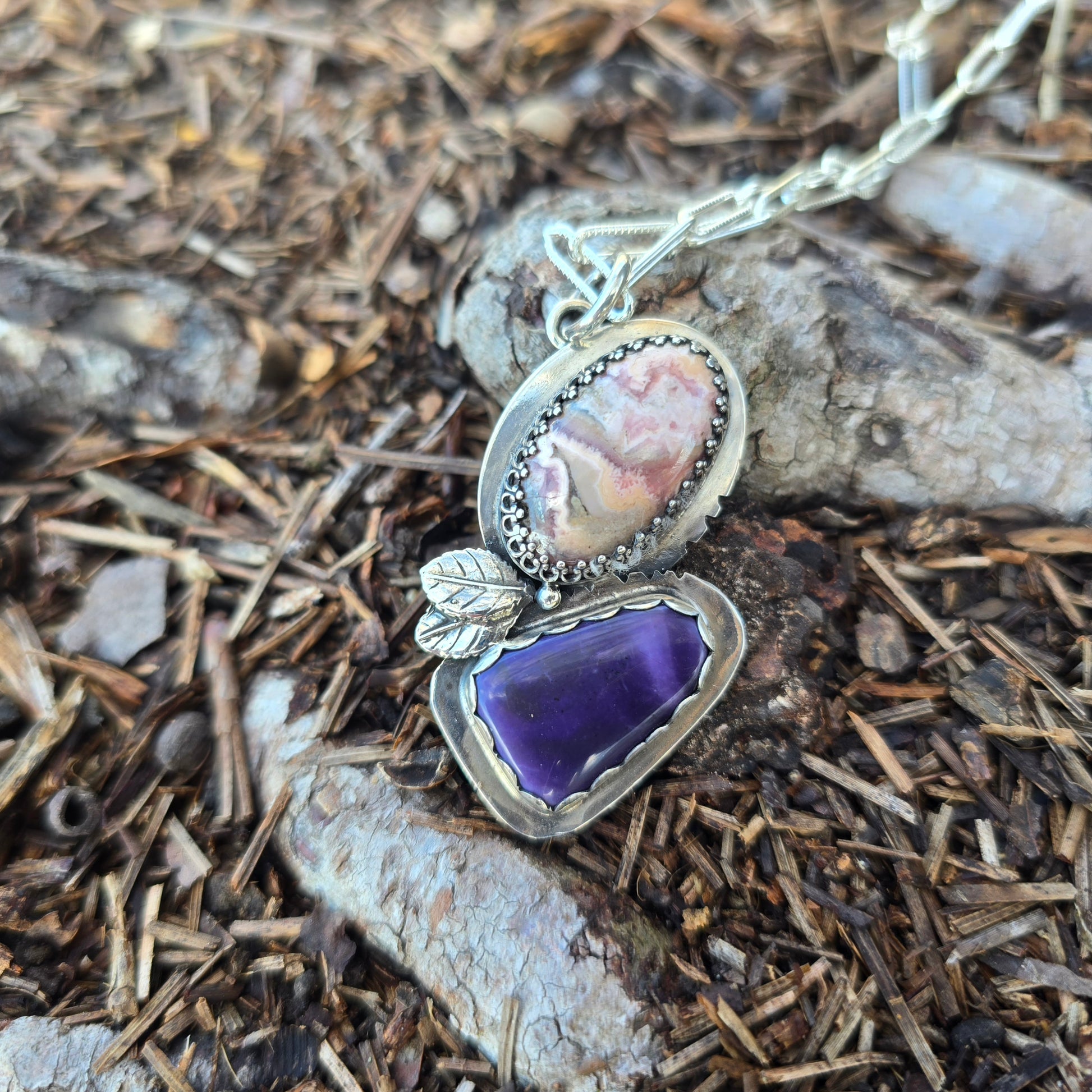 sterling silver leaf pendant with purple and pink stones displayed on ground
