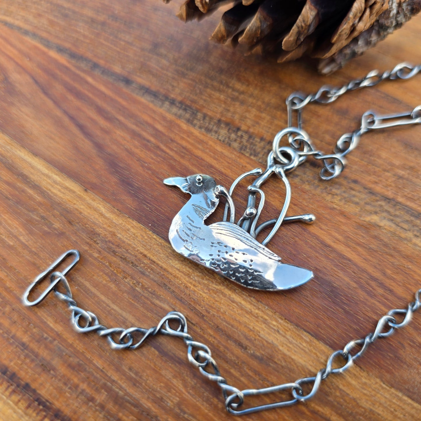Silver adirondack loon pendant necklace on a wooden surface