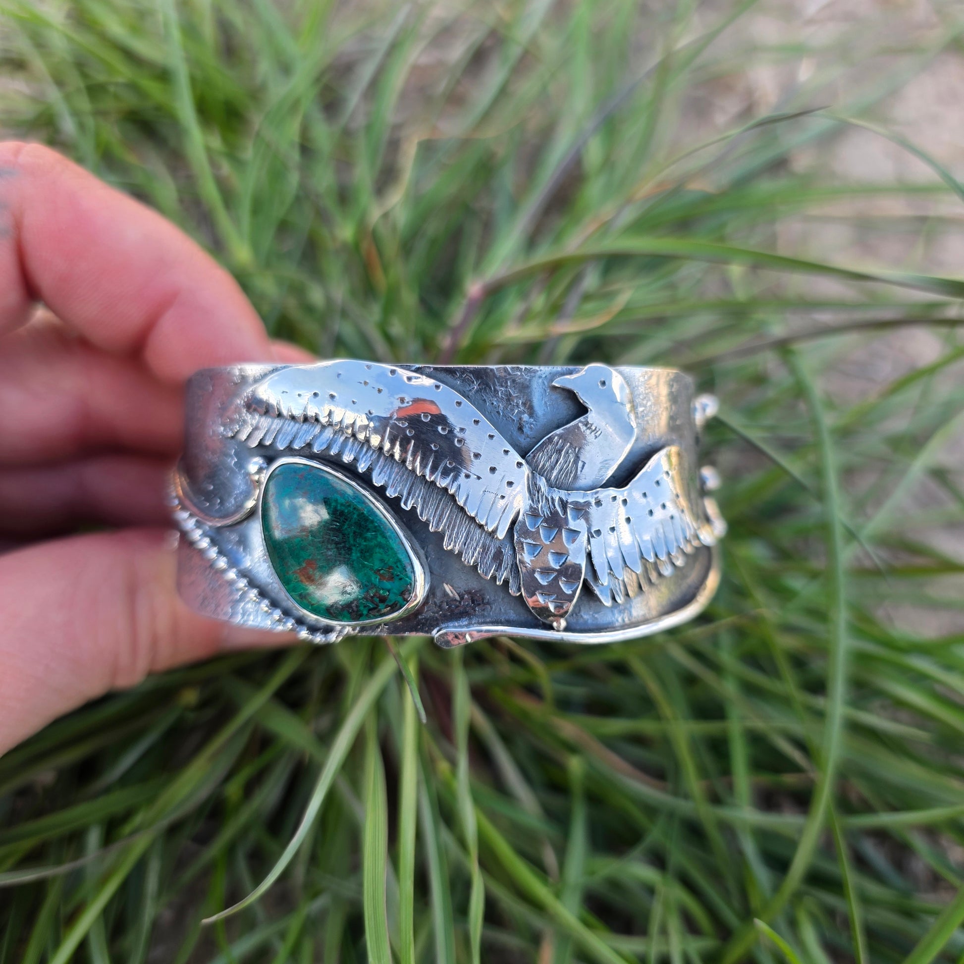 Sterling silver loon in flight bracelet with green stone being held by hand