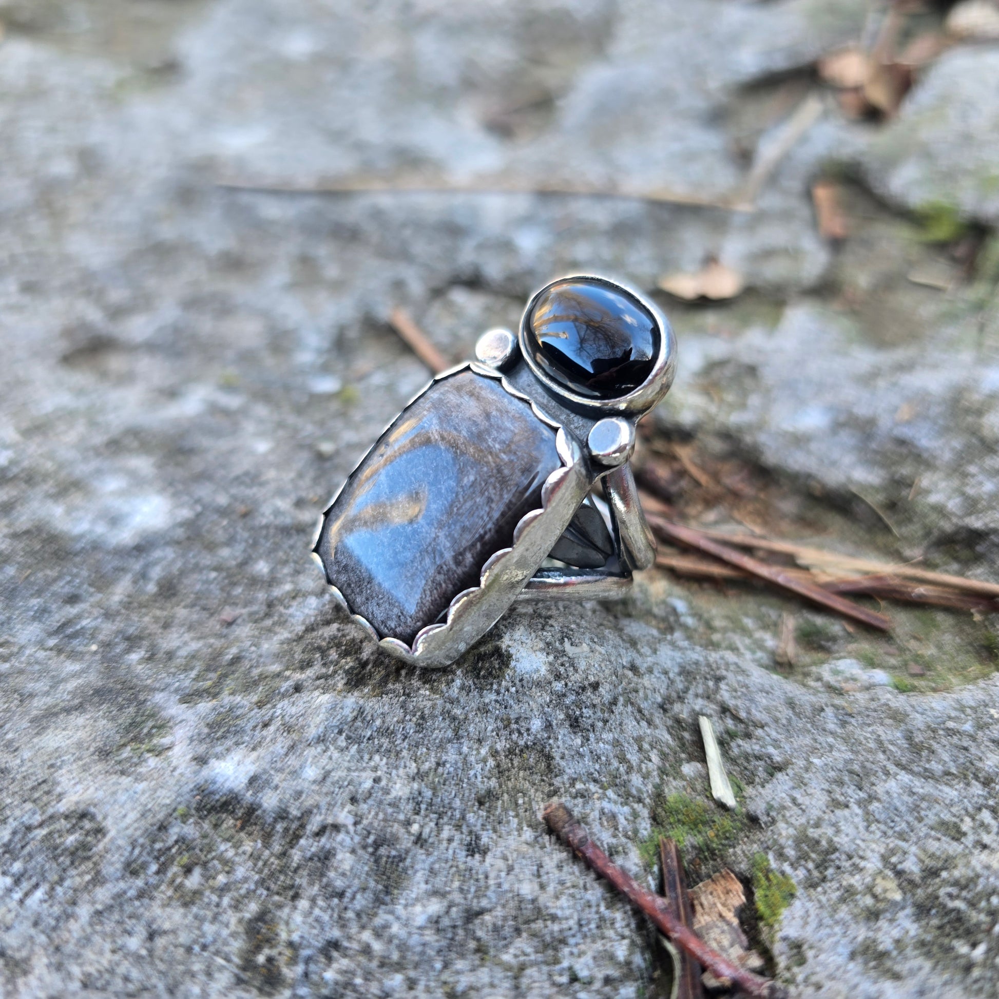 silver statement ring with obsidian and black onyx displayed on rock