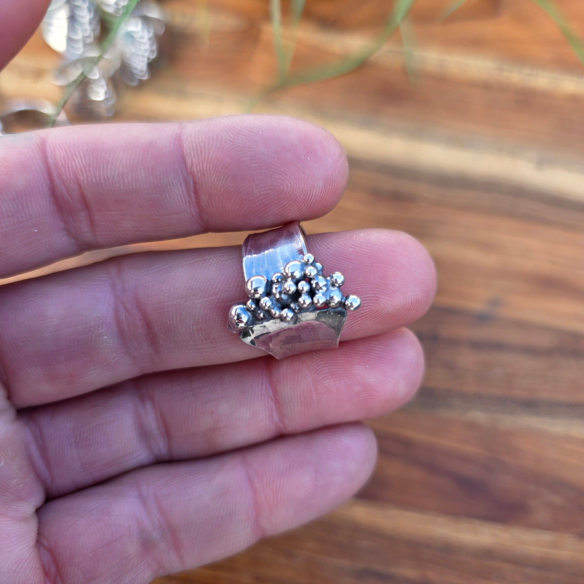 Silver ring with bead details on a finger against a blurred natural background