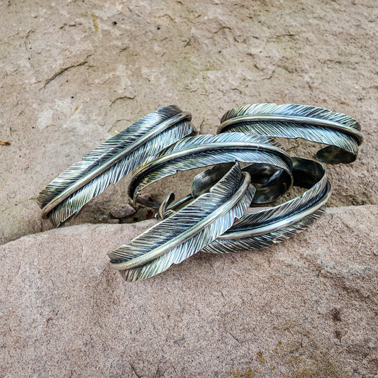 collection of sterling silver feather cuff bracelets on rock